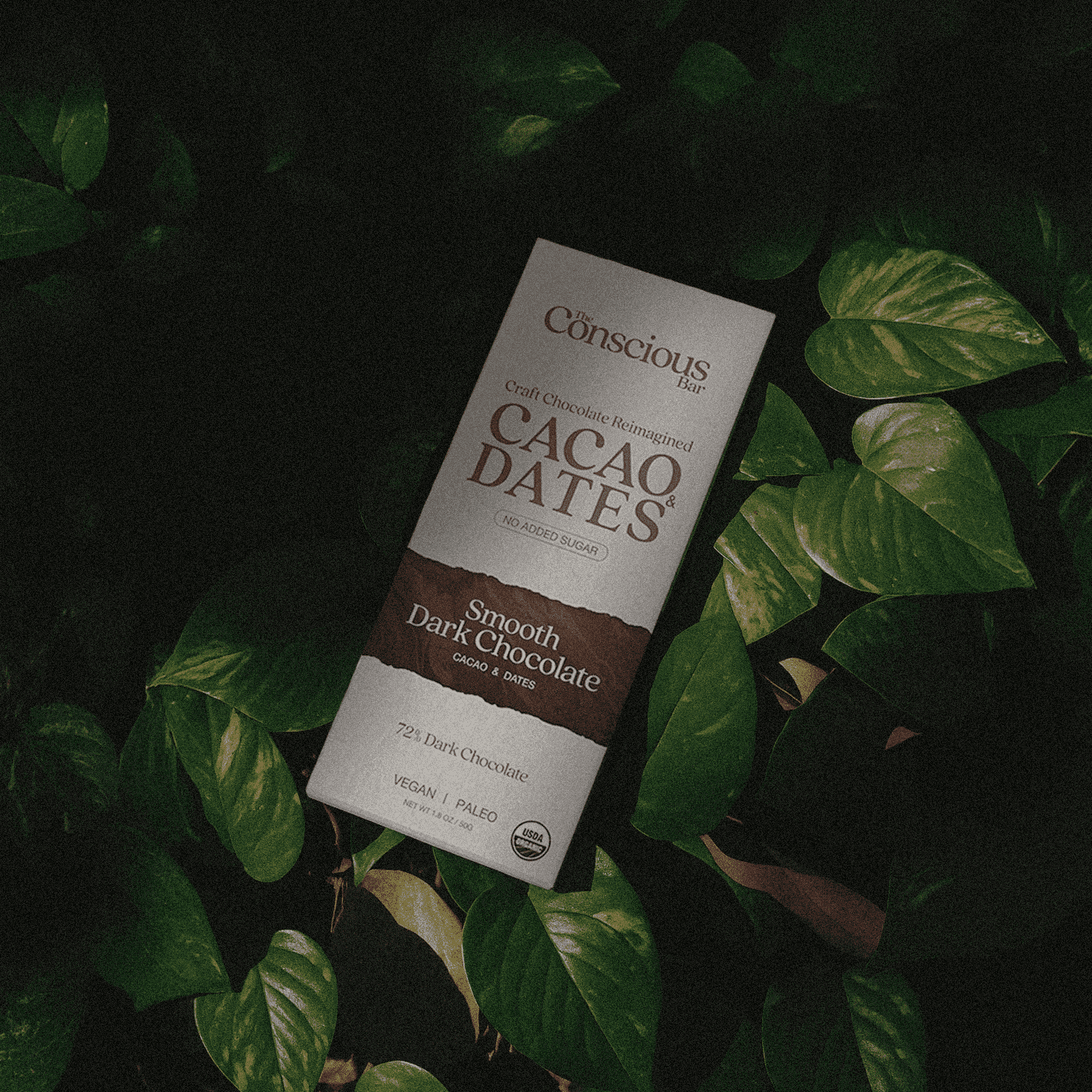 Conscious Bar Cacao Dates chocolate bar on a leafy background