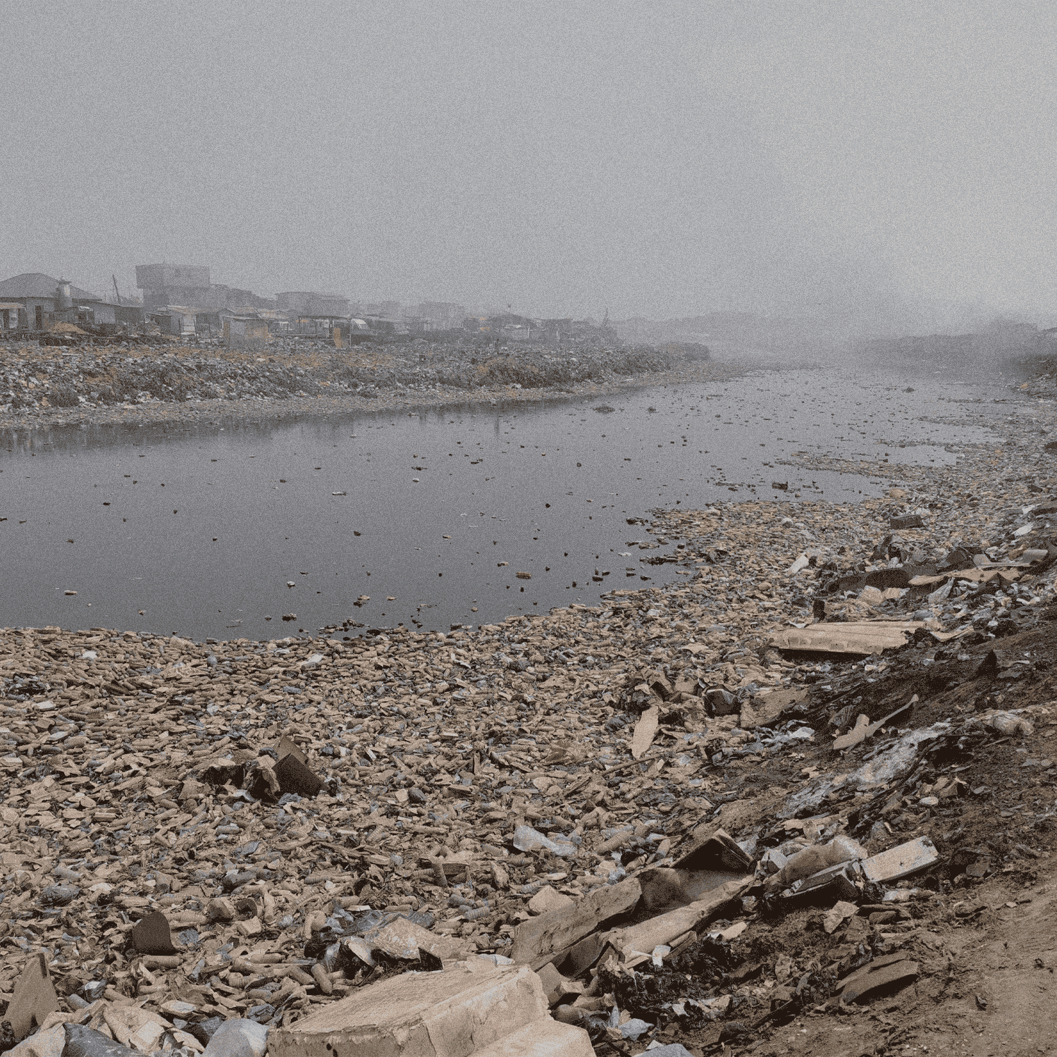 Polluted river with garbage and debris, surrounded by industrial buildings on a foggy day.